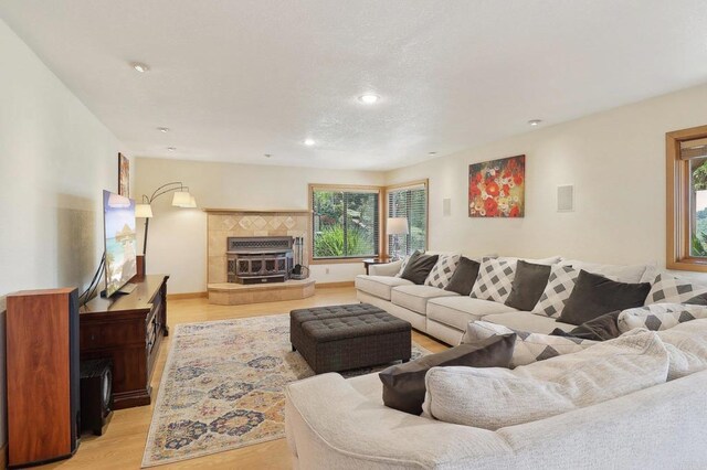 living room featuring a tiled fireplace, recessed lighting, baseboards, and light wood-type flooring