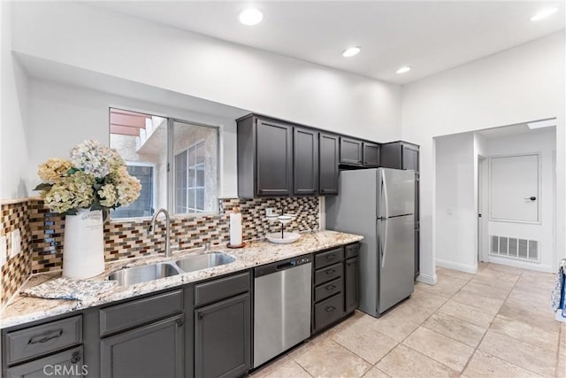 kitchen with visible vents, decorative backsplash, light stone countertops, a sink, and appliances with stainless steel finishes