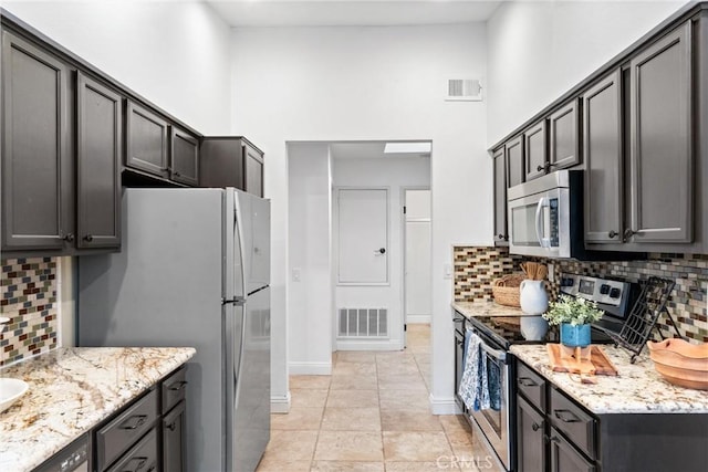 kitchen featuring a high ceiling, appliances with stainless steel finishes, light stone counters, baseboards, and decorative backsplash