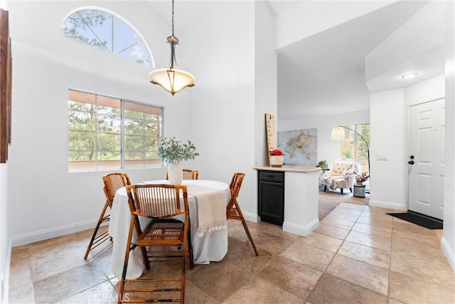 dining space with stone tile floors, baseboards, plenty of natural light, and a high ceiling