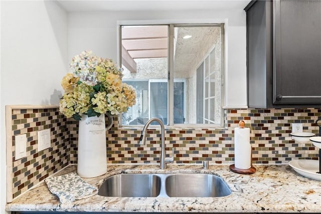 interior details with light stone counters, a sink, and tasteful backsplash