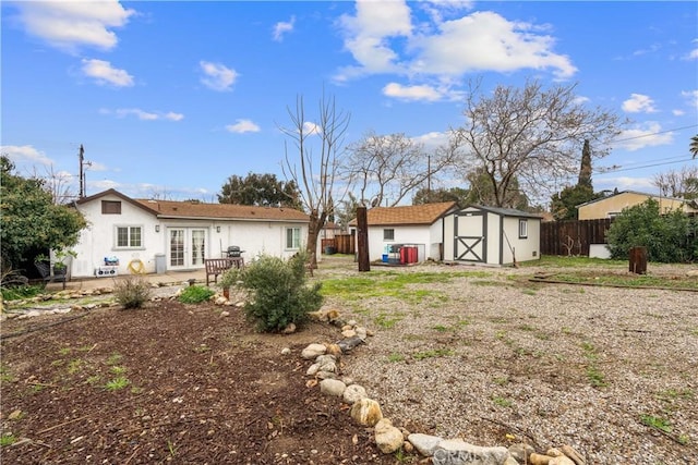 rear view of property with fence, stucco siding, a shed, french doors, and an outdoor structure