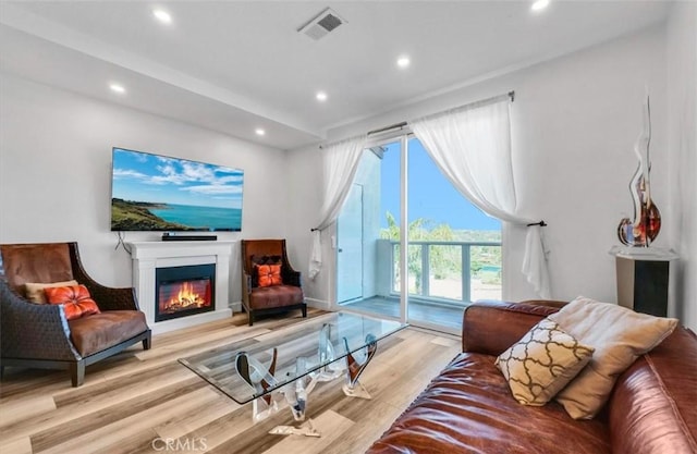 living room with recessed lighting, visible vents, a glass covered fireplace, and light wood finished floors