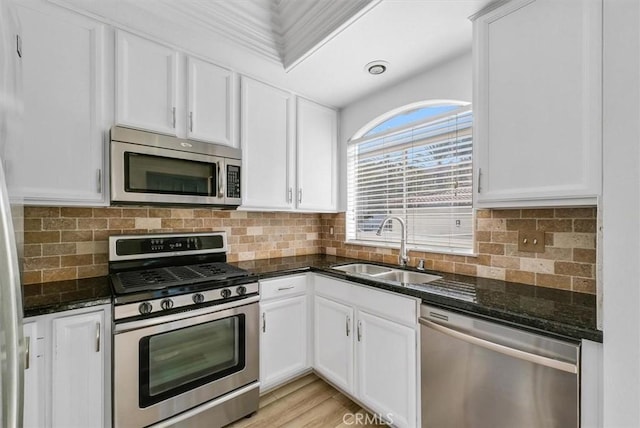 kitchen featuring appliances with stainless steel finishes, a sink, dark stone countertops, white cabinetry, and decorative backsplash