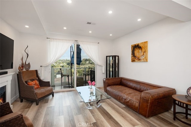 living room with recessed lighting, a lit fireplace, visible vents, and light wood-style floors