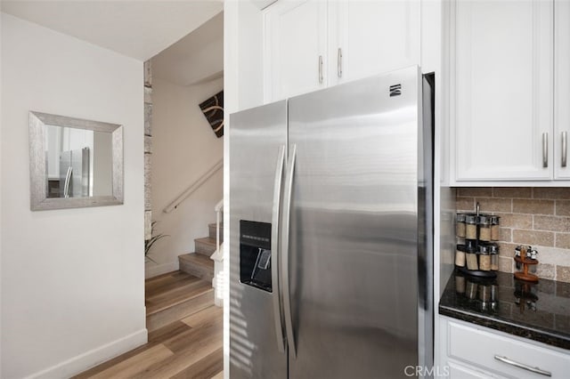 kitchen featuring freestanding refrigerator, stainless steel fridge, dark stone counters, white cabinetry, and backsplash