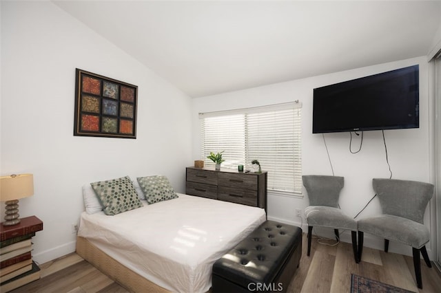 bedroom featuring baseboards, wood finished floors, and lofted ceiling