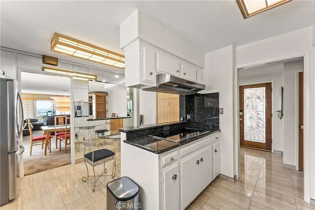 kitchen featuring white cabinets, black electric stovetop, freestanding refrigerator, light tile patterned floors, and under cabinet range hood