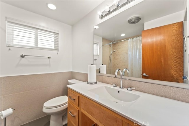 bathroom featuring tile walls, curtained shower, a wainscoted wall, vanity, and toilet
