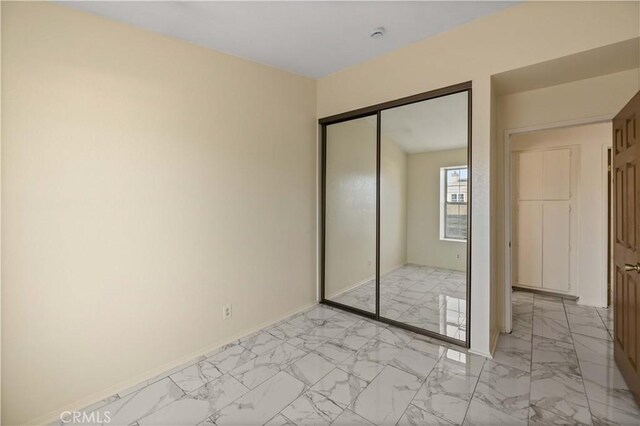 unfurnished bedroom featuring baseboards, marble finish floor, and a closet