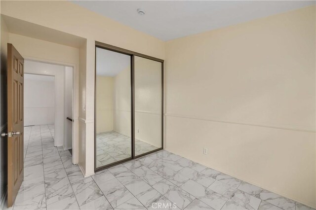 unfurnished bedroom with marble finish floor and a closet