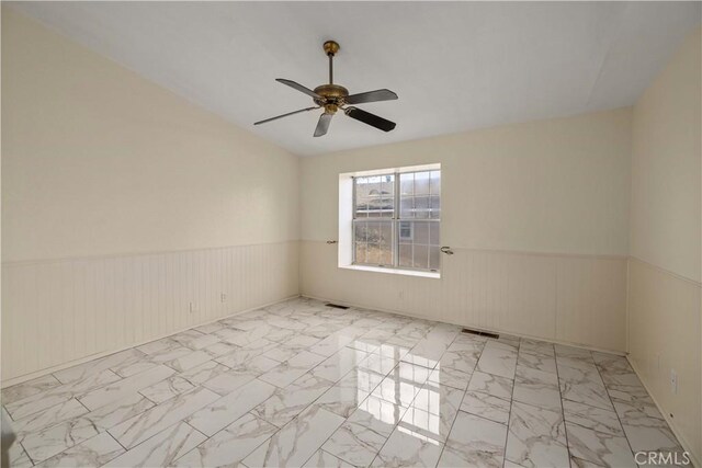 unfurnished room featuring a ceiling fan, visible vents, marble finish floor, and a wainscoted wall