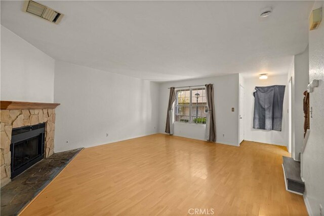 unfurnished living room with visible vents, a stone fireplace, and wood finished floors