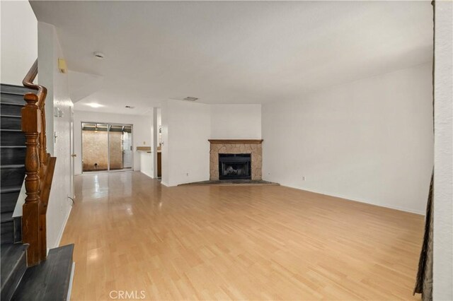 unfurnished living room with light wood-style floors, stairs, baseboards, and a stone fireplace