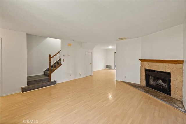 unfurnished living room featuring visible vents, wood finished floors, a fireplace, and stairway