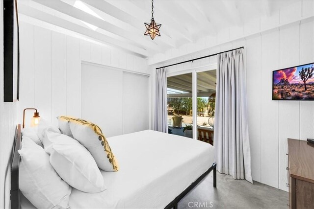 bedroom featuring access to outside, concrete floors, beam ceiling, and a closet