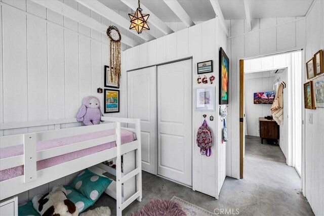 bedroom with a closet, wood walls, concrete floors, and beamed ceiling