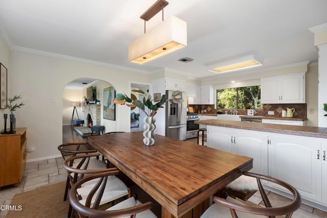 dining area with crown molding, arched walkways, visible vents, and stone tile flooring