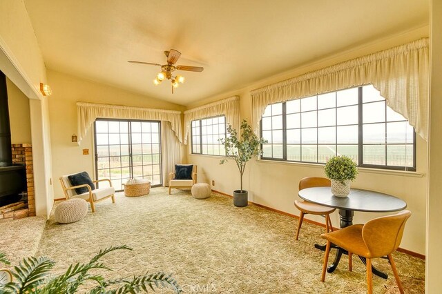 sitting room featuring a wood stove, carpet floors, a ceiling fan, baseboards, and vaulted ceiling