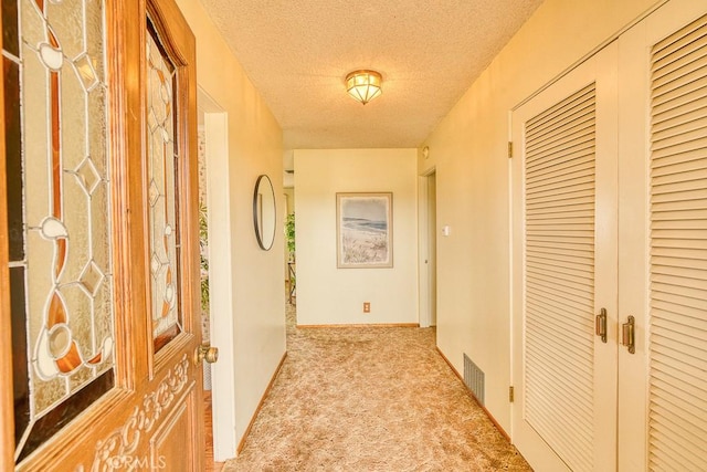 hallway featuring carpet flooring, a textured ceiling, and visible vents