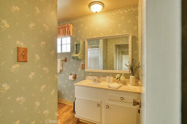 bathroom featuring baseboards, wallpapered walls, wood finished floors, and vanity