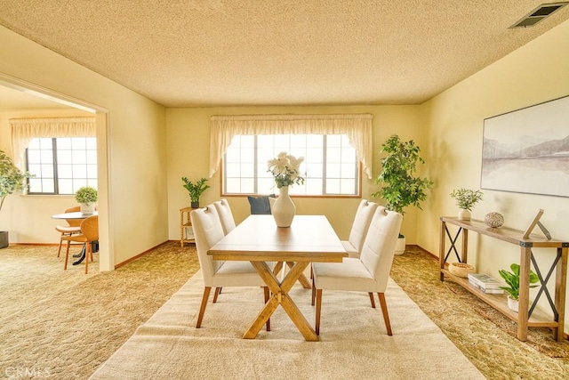 carpeted dining space featuring plenty of natural light, a textured ceiling, and visible vents