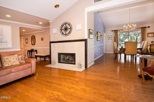 living area with crown molding, a notable chandelier, a fireplace, wood finished floors, and lofted ceiling