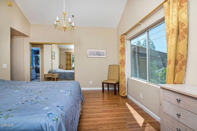 bedroom featuring a closet, lofted ceiling, wood finished floors, baseboards, and a chandelier