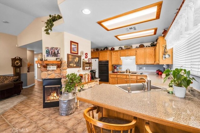 kitchen with dobule oven black, a peninsula, under cabinet range hood, a sink, and vaulted ceiling