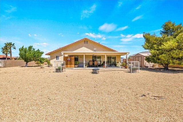 rear view of house featuring fence, a storage unit, stucco siding, a patio area, and an outdoor structure
