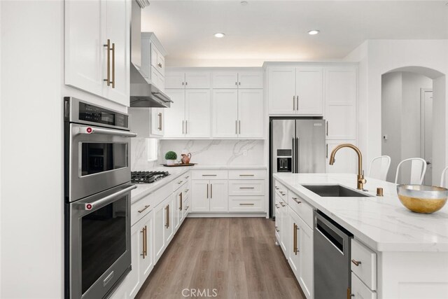 kitchen with appliances with stainless steel finishes, a sink, arched walkways, white cabinetry, and a center island with sink