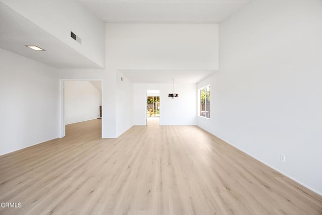 unfurnished living room featuring visible vents, a chandelier, light wood finished floors, and a towering ceiling