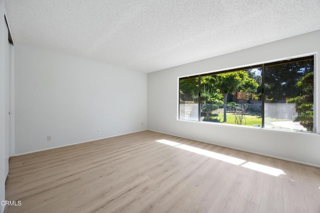 empty room with a textured ceiling, baseboards, and light wood finished floors