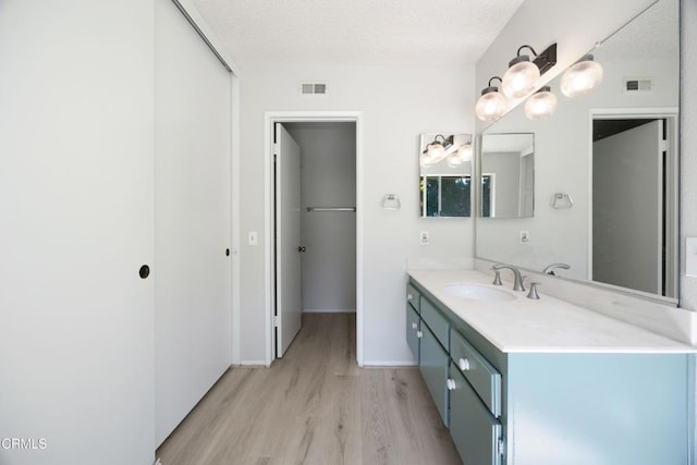 bathroom with a textured ceiling, visible vents, wood finished floors, and vanity
