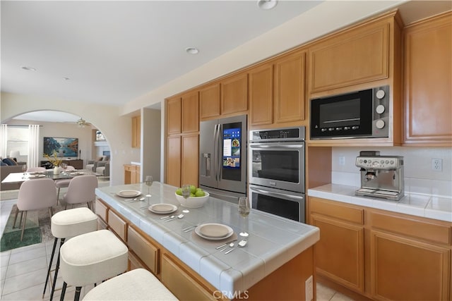 19131 Camassia Ct, Riverside, CA 92508 - kitchen featuring tile counters, stainless steel appliances, arched walkways, and light tile patterned floors