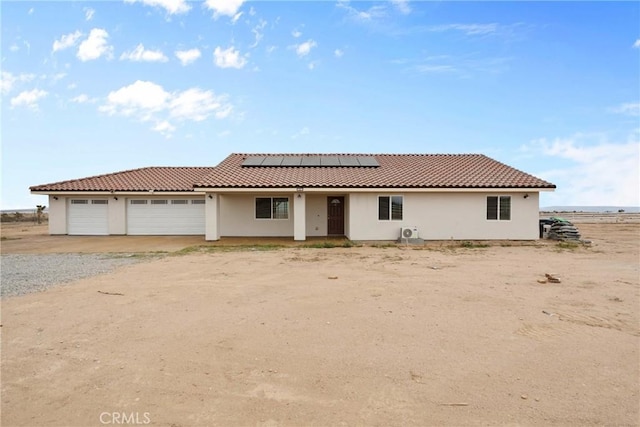 12185 Atsina Rd, Phelan, CA 92371 - view of front of home featuring a tiled roof, solar panels, dirt driveway, an attached garage, and stucco siding