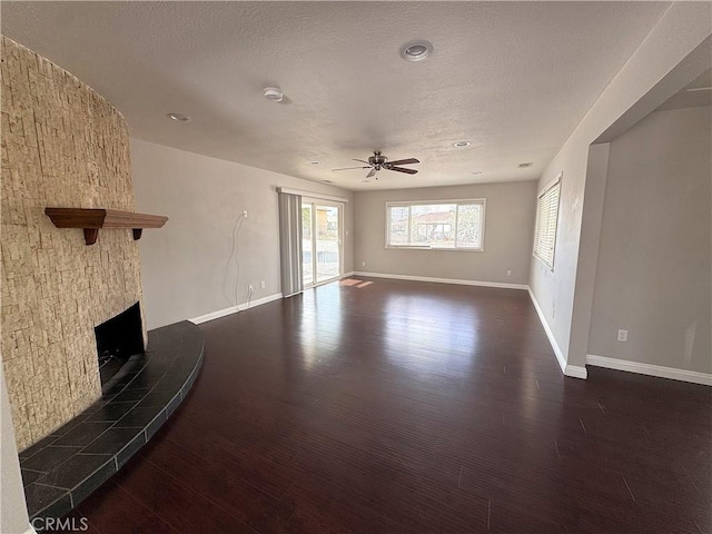 unfurnished living room with wood finished floors, a fireplace, baseboards, ceiling fan, and a textured ceiling