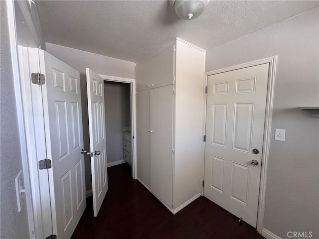 hall featuring a textured ceiling, baseboards, and dark wood finished floors