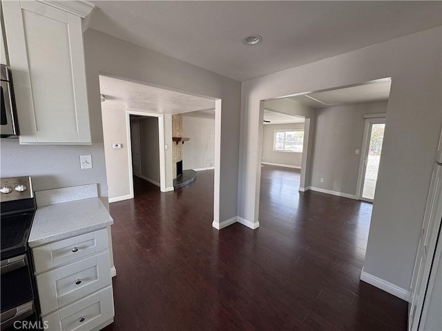 kitchen with baseboards, white cabinets, electric range oven, and dark wood-type flooring