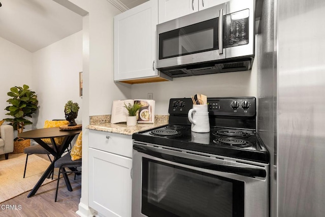 kitchen featuring white cabinets, electric range, light stone countertops, light wood finished floors, and stainless steel microwave