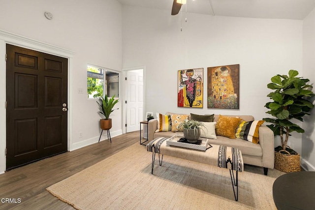 living area with baseboards, ceiling fan, wood finished floors, and a high ceiling
