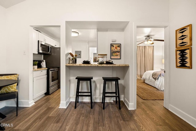 kitchen featuring appliances with stainless steel finishes, a breakfast bar, dark wood finished floors, and white cabinetry
