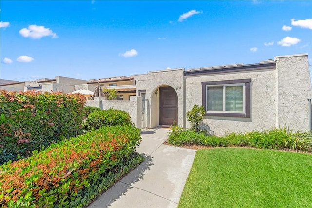 view of front facade featuring stucco siding, fence private yard, and a front lawn