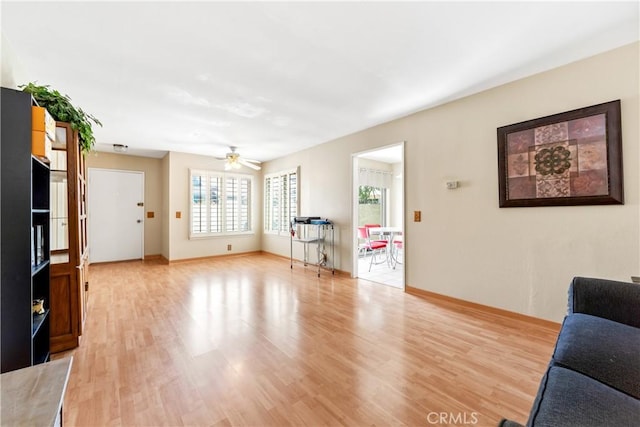 living area with baseboards, a ceiling fan, and light wood-style flooring