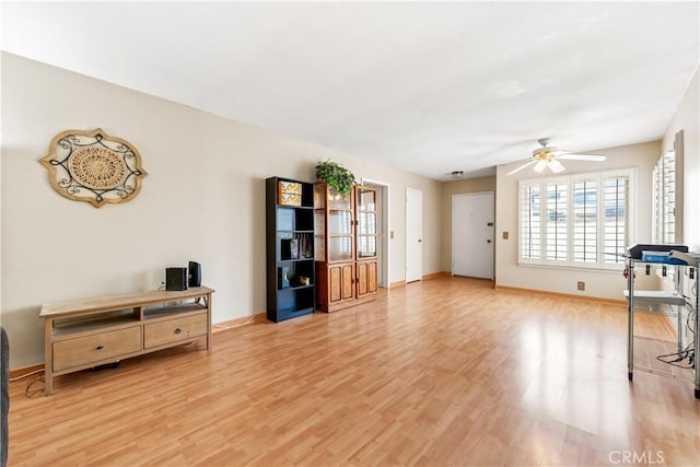 living area featuring ceiling fan, baseboards, and light wood-type flooring