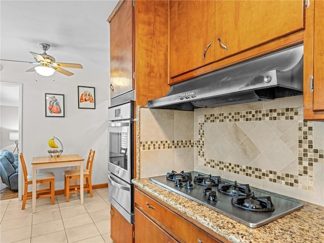 kitchen with brown cabinetry, a warming drawer, backsplash, light tile patterned floors, and stainless steel appliances