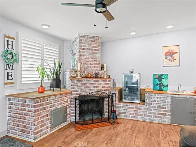 living area featuring a brick fireplace, wood finished floors, beverage cooler, recessed lighting, and a ceiling fan
