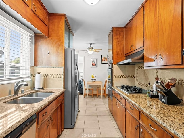 kitchen featuring under cabinet range hood, appliances with stainless steel finishes, brown cabinetry, and a sink
