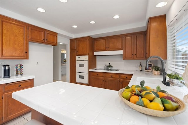 kitchen with white double oven, brown cabinetry, a peninsula, and a sink
