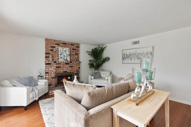 living area with a brick fireplace, visible vents, and wood finished floors